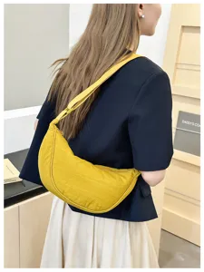 Detailed view of the yellow crescent shoulder bag worn by a model in a clean indoor setting.