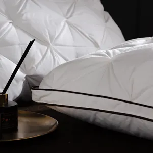 Detailed view of luxury white down pillow with elegant twist pleats and brown piping.