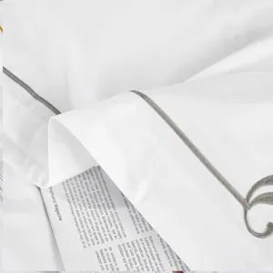 White sateen hotel bedding set detail with elegant gray embroidery and piping trim.