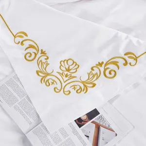 White sateen bedding detail with elegant gold embroidery, luxury hotel style cotton sheet.