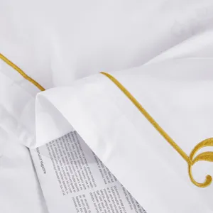 Close-up detail of white cotton hotel bedding featuring elegant gold piping and delicate embroidery.