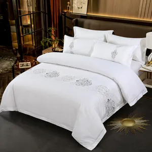 Detail view of luxury white cotton bedding set with elegant grey embroidery in bedroom.