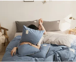 Cozy cotton bedding set scene detail, soft blue and grey pillows on comfortable bed.