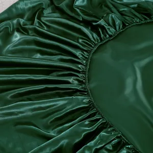 Detalle de la sábana bajera de satén de seda verde oscuro con tela lisa y borde elástico.