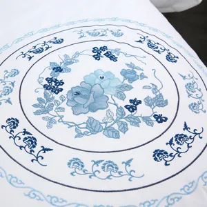 Close-up detail of white cotton bedding featuring exquisite blue floral embroidery.