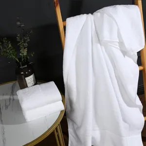 Hotel white cotton bath towel set displayed on ladder and table for home or salon use.