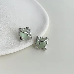 Close-up of minimalist liquid-shaped silver earrings with micro-inlaid zircon and green stone.