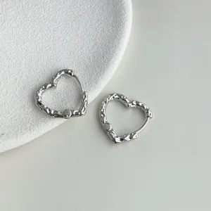 Close-up detail of irregular heart-shaped silver hoop earrings on white textured display pad.