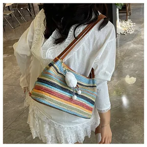 Detailed shot of a colorful straw woven shoulder bag featuring vibrant rainbow stripes and cute plush pendant.
