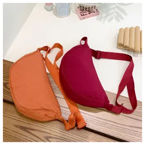 Close-up detail of stylish crescent crossbody bags in orange and burgundy with adjustable straps.