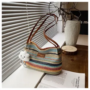 Detail view of colorful woven straw shoulder bag with cute cloud keychain and leather straps.