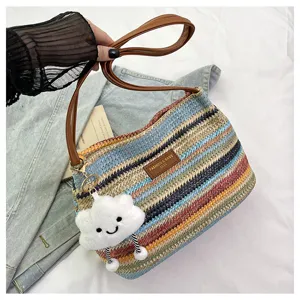 Detail view of colorful woven straw shoulder bag with cute cloud charm and brown leather strap.