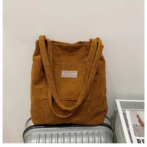 Corduroy tote bag detail showing soft fabric texture, front pocket and fashion label.