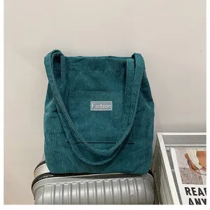 Corduroy tote shoulder bag detail view, dark green fabric with front pocket and fashion label.