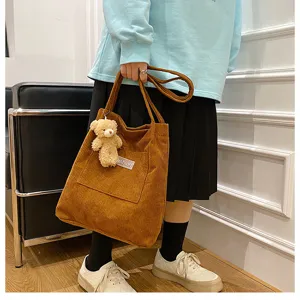 Detail shot of vintage corduroy shoulder tote bag with cute bear pendant and front pocket design.