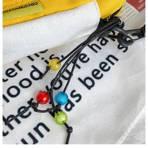 Dettaglio borsa di tela, tessuto giallo e bianco con cordini neri e perline colorate decorative.