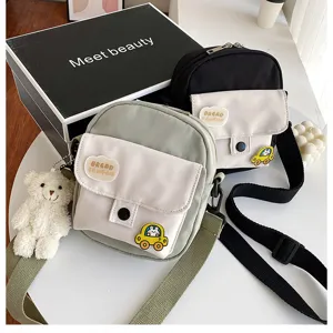 Detailed view of canvas crossbody bags in green and black with cute bear pendant and patches.