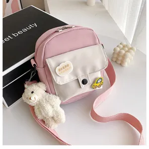 Pink canvas crossbody bag with white front pocket and cute bear pendant for daily use.