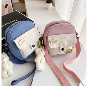 Cute Korean style canvas crossbody bag for girls with cute bear pendant and front pocket design.