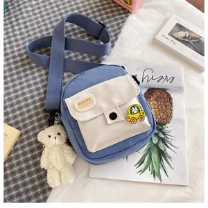 Canvas crossbody bag detail showing blue fabric, white front pocket, plush bear and cute car badge.