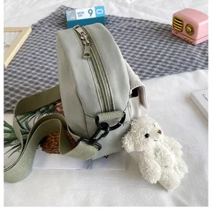 Detailed view of the sage green canvas crossbody bag with cute fluffy bear pendant.
