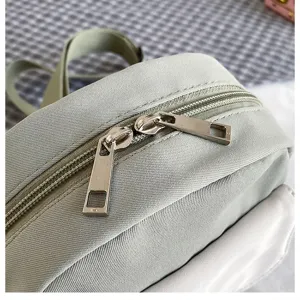Close-up detail of green canvas crossbody bag with smooth double zippers and durable metal pulls.