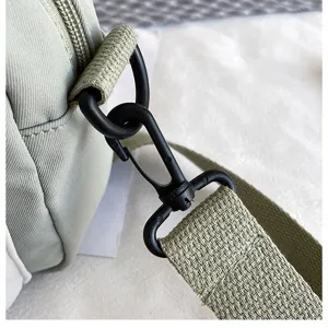 Close-up detail shot of green canvas crossbody bag strap buckle and durable metal clip.