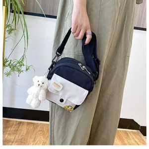 Close-up detail of the black and white canvas crossbody bag with cute plush bear pendant.