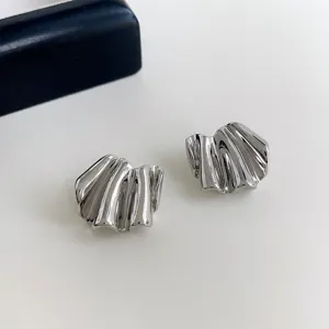 Dettaglio in primo piano di orecchini geometrici plissati in metallo argentato lucido.