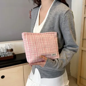 Pink tweed cosmetic pouch detail showing textured fabric and small brand label on hand.