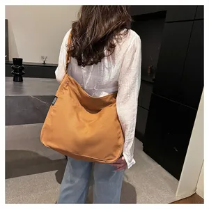 Detail shot of a casual brown canvas tote bag worn by a model in a modern room setting.