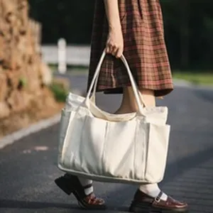 Detailed view of casual white canvas tote bag with multiple pockets and durable dual handles.
