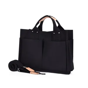 Detail view of black canvas tote bag with front pockets and durable leather handles.