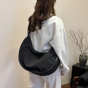 Detailed view of a minimalist black hobo crescent shoulder bag, worn casually by a model.