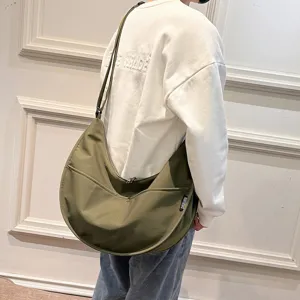 Detailed shot of a casual olive green canvas crescent crossbody bag worn by model.