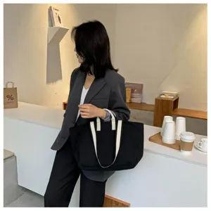 Detailed view of a simple large capacity black canvas tote bag with white straps in a cafe.