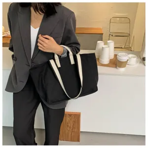 Detail view of a stylish black canvas tote bag with white straps carried in a chic cafe setting.