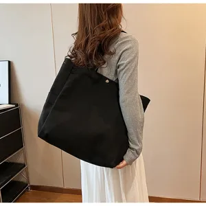 Detailed shot of a large black canvas tote shoulder bag worn by a model for daily use.
