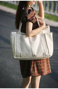 Detail view of a large beige canvas tote bag with multiple outer pockets and dual shoulder straps.