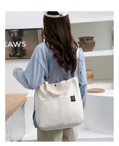 Casual minimalist white canvas shoulder bag with crossbody strap and front pocket detail.