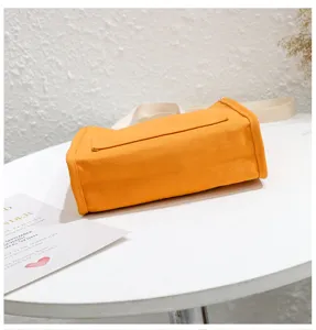 Close-up detail of orange canvas bento shoulder bag placed on white table, textured surface.