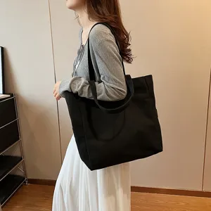 Detail view of the black canvas shoulder tote bag worn by model, large capacity commuter style.