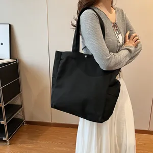 Detail view of a large black canvas tote bag worn by a model, perfect for daily commuting.