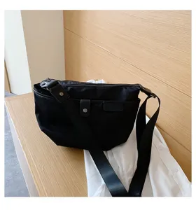 Black nylon crossbody bag detail showcasing durable fabric, wide shoulder strap and pocket.