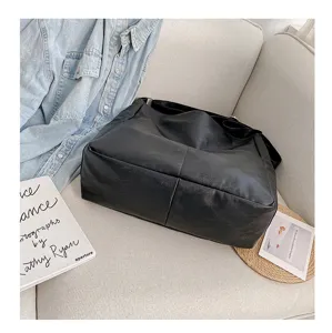 Detail view of a black PU leather slouchy shoulder bag with stitching on a cozy sofa.