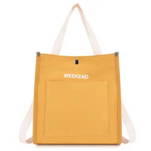 Yellow canvas tote bag front pocket detail view featuring white straps and weekend print.