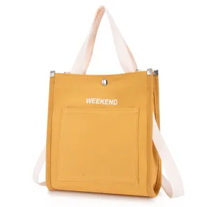 Close-up of yellow canvas tote bag with front pocket, white straps, and detailed view.