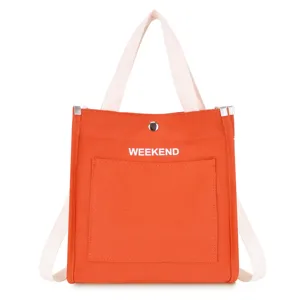 Orange canvas tote bag front pocket detail with white handles and weekend text print.