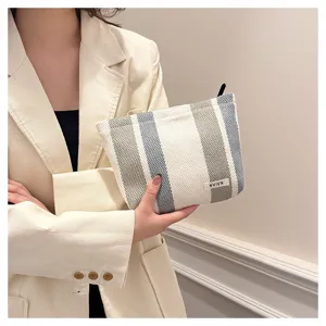 Detail shot of a stylish striped linen cosmetic bag, portable travel pouch with zipper and label.