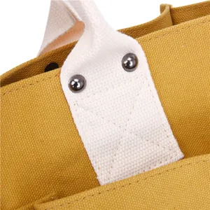 Close-up detail of yellow canvas bag handle featuring white webbing and metal rivets.